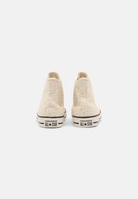 Pár krémových Converse All Star vysokých tenisek s květinovým vzorem na okrajích, pohled zezadu na bílém pozadí.