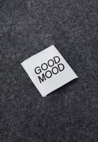 Hall jooksva halli kangaga, mille küljes on valge silt, millel on julged mustad tähed "GOOD MOOD". Tekstuur näib olevat pehme ja diskreetne.