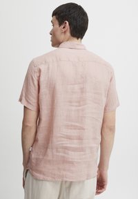 Lichtroze shirt met korte mouwen van linnen, met een subtiele textuur en een klassieke kraag. De achterkant heeft een rechte zoom en minimale details.