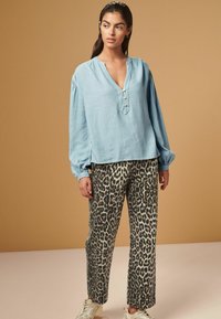 Lichtblauwe linnen blouse met een V-hals, knoopdetails en pofmouwen, gecombineerd met een losse leopardprint broek.