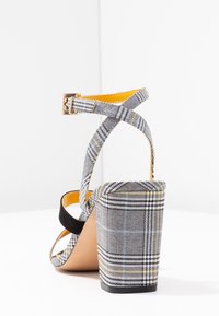 Rutigt blockklackssandalett med ett grått, svart och gult mönster, med korsade remmar och detaljer i guldton.