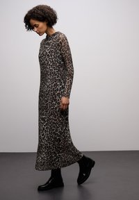 Šaty s leopardím potiskem dlouhý rukáv z průsvitné látky, s přiléhavým korzetem a splývavou sukní, doplněné černými kotníkovými botami.