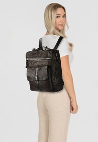 Mochila de cuero negro con múltiples bolsillos, acabado texturizado, correas ajustables y una asa superior. Gran bolsillo frontal con solapa.