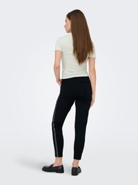 Black tapered pants with a glossy stripe down the sides, paired with a light green short-sleeve top, viewed from the back.