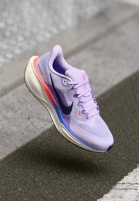 Heled lilla jooksu king, millel on võrgust pealis, must swooshi logo, roosa ja sinise aktsentidega, pehmendatud soe ja sile, aerodünaamiline kuju.