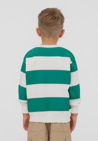 Felpa a righe verdi e bianche realizzata in tessuto morbido, con scollatura rotonda e vestibilità ampia, abbinata a pantaloni corti beige.