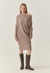 Übergrößen, schulterfreies Strickkleid aus weichem, flauschigem braunem Material mit langen Ärmeln und geripptem Saum, kombiniert mit knielangen braunen Lederstiefeln.