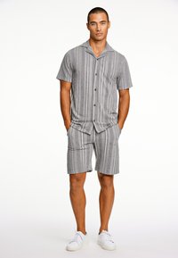Grijs gestreept set van een T-shirt met korte mouwen en shorts, met een kraag, knopen en lichte stof. Gecombineerd met witte sneakers.
