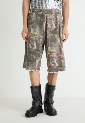 Shorts mimetici con orlo sfrangiato, realizzati in tessuto testurizzato. Abbinati a stivali neri al ginocchio con fibbie e suola robusta.
