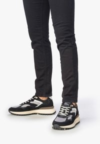 Sneaker nere e grigie con parte superiore in mesh e suede, suola bianca spessa e suola esterna in gomma nera, con chiusura a laccio e accenti di logo discreti.