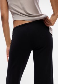 Calças de lounge pretas com um tecido texturizado, apresentando uma cintura elástica. Uma parte superior cinza claro cobre parcialmente a cintura nas costas.