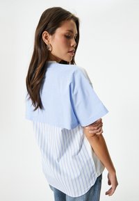 Korte mouwen shirt met een lichtblauwe gestreepte bovenkant en een witte, verticaal gestreepte onderkant. Zachte stof met een relaxte pasvorm.