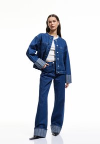 Jeansjacka i avslappnad passform, med ljusblå foder i ärmarna, kombinerat med högmidjade jeans, båda i mörkblått. Klassiska knappränder.