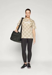 Beige mønstrete T-skjorte med logo, svarte leggings og svart treningsbag, kombinert med svarte og rosa sportsko. Rent design og sporty stil.