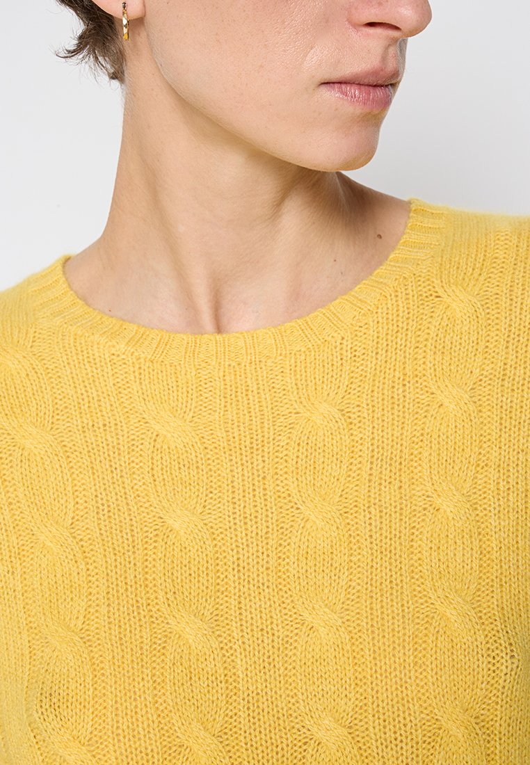Żółty sweter dziewiarski z wzorem w warkocze, okrągłym dekoltem i miękką teksturą, ukazujący zbliżenie detali odzieży.