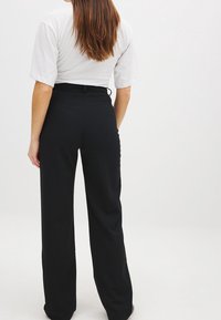 Hoch taillierte schwarze Hosen mit weit geschnittenem Design, versehen mit einer glatten Textur und minimalen Nähdetails, kombiniert mit einem einfachen weißen T-Shirt.