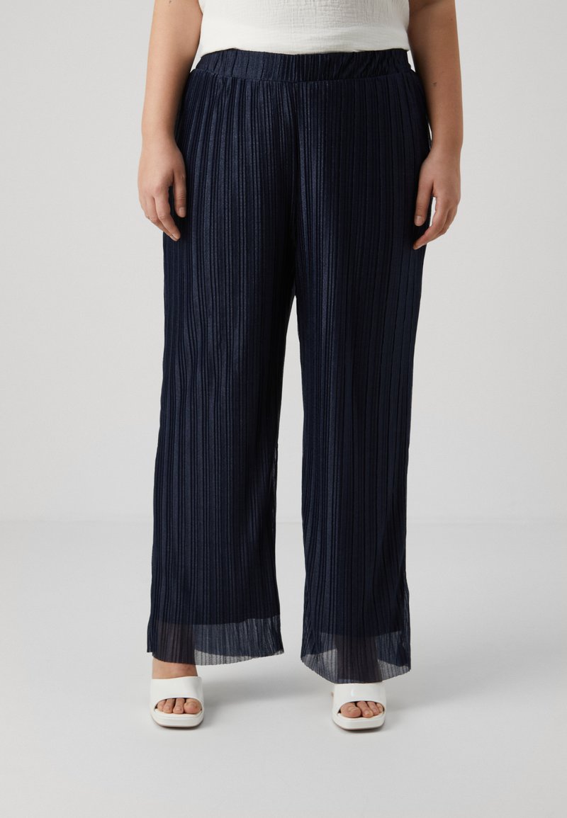Navy pleated wide-leg pants with an elastic waistband, textured fabric, and sheer accents at the hem. Styled with white open-toe heels.