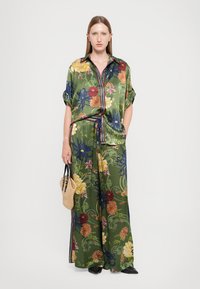 Cămașă din mătase verde cu flori și pantaloni largi, având flori vibrante și modele răsucite. Asortată cu o geantă texturată.