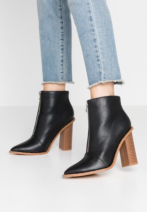 Bottines en cuir noir avec zip avant et talons blocs en bois empilés, portées avec un jean bleu clair à ourlet effiloché.