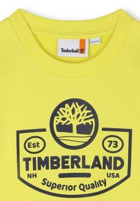Sweatshirt en coton jaune avec un col rond côtelé, arborant un logo Timberland bleu et l'année d'établissement "73" imprimée sur le devant.