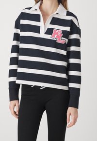 Jersey de rayas azul marino y blanco con un cuello blanco y un logo bordado en rosa "KL" en el pecho. Cuenta con mangas largas y un corte holgado.
