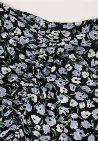 Mustapohjainen kangas, jossa on satunnaisesti sijoitettu vaaleansininen ja valkoinen kukkakuvio. Kerrostettu tekstuuri kaula-aukon lähellä vihreillä lehtikoristeilla.