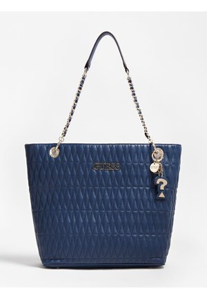 Granatowa pikowana skórzana torebka Guess z łańcuszkowym paskiem na ramię i metalowymi zawieszkami z logo, w tym znakiem zapytania.