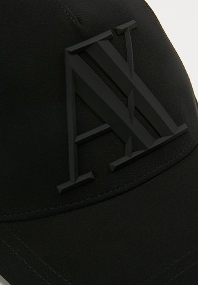 Casquette noire avec un logo "AX" en relief bien visible en noir mat, fabriquée en tissu avec une texture lisse et une visière courbée.