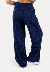Persona che indossa pantaloni blu navy ampi con motivo leopardato scuro, abbinati a scarpe da ginnastica bianche.