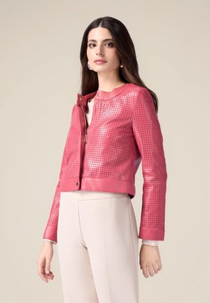 Cropped pink leather jacket with perforated design, zip closure, and contrasting cuffs. Paired with light beige trousers.