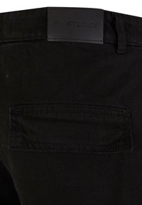 Pantalons en denim noir avec une poche arrière et une taille lisse et texturée, ornée d'une étiquette noire en relief portant la mention "2Y STUDIOS."