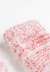 Calzini lavorati a maglia in rosso e bianco, caratterizzati da una consistenza morbida e pelosa con un motivo a strisce. Forma arrotondata con un bordo superiore elasticizzato.