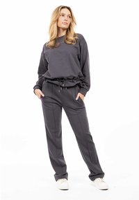 Set di felpa grigia scura e pantaloni jogger realizzato in tessuto morbido. L'outfit presenta una vestibilità rilassata, vita elasticizzata e dettagli con coulisse.