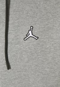 Felpa grigia con tessuto strutturato, caratterizzata da un logo Jumpman ricamato in bianco e nero e dettagli con coulisse nere.