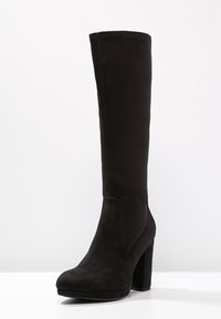 Černé kozačky po kolena vyrobené z měkkého semiše, s robustním vysokým podpatkem a hladkým, bezproblémovým designem bez viditelného hardwaru či akcentů.