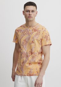 Camiseta de manga corta y cuello redondo en color naranja con un estampado audaz de hojas tropicales en amarillo y blanco. Fabricada con tela ligera y suave.