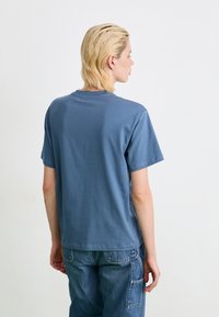 T-shirt in cotone blu con collo a giro, maniche corte e vestibilità rilassata. Il retro è semplice con una texture liscia, abbinato a pantaloni cargo in denim.