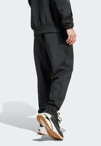 Black sweatshirt and pants made from smooth fabric. Pants feature an elastic waistband; shoes have a black and white design with a gum sole.