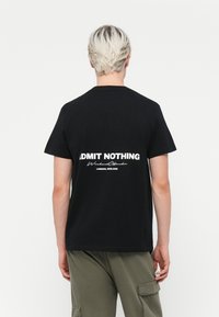 Zwarte katoen t-shirt met opvallende witte tekst op de achterkant: "ADMIT NOTHING" en "WeekendOffender, LONDON, ENGLAND." Korte mouwen, klassieke pasvorm.
