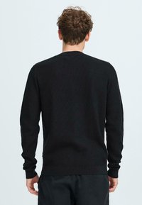Schwarz gerippter Strickpullover mit langen Ärmeln und Rundhalsausschnitt, ausgestattet mit einer strukturierten Oberfläche und dezenten Seitennahtdetails.
