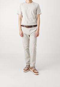 Helles graues Baumwoll-T-Shirt, hellbeige Chinos, brauner Leder-Gürtel und braune Sneakers mit einer weißen Sohle und grauen Schnürsenkeln.
