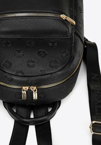 Zaino in pelle nera testurizzata con forma rotonda, hardware della cerniera dorato e un motivo impresso. Presenta spallacci regolabili e un manico superiore.
