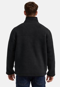 Chaqueta de forro polar negra con un collar alto, tela texturizada, un acabado suave y un dobladillo recto, vista desde la parte trasera.