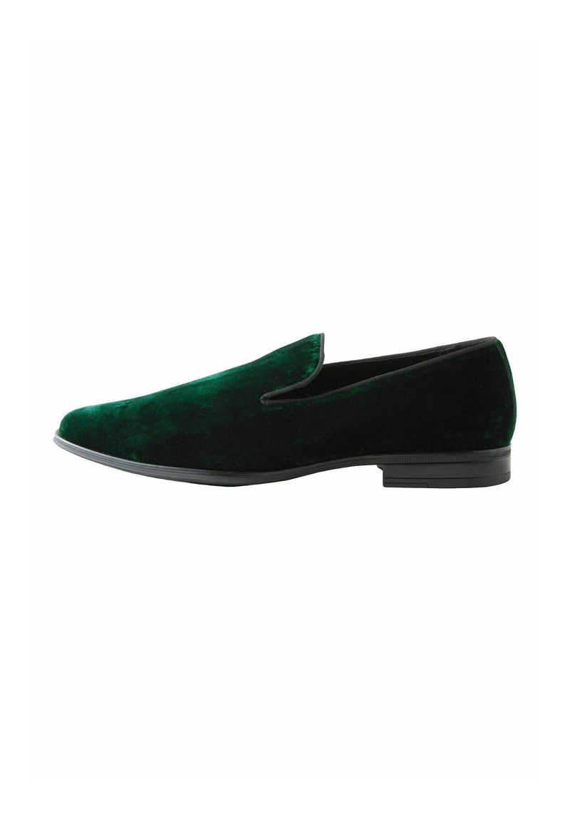 Green velvet slip-on shoe with a black rubber sole, featuring a smooth texture and minimalistic design, angled for side view.