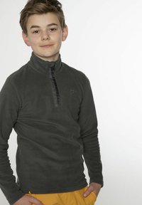 Pullover in pile di carbone con colletto zip, caratterizzato da hardware nero e dettaglio del logo, indossato sopra pantaloni gialli su uno sfondo neutro.