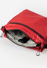 Borsa rossa in nylon con texture liscia e finitura impermeabile, dotata di chiusura a zip e interno grigio con una tracolla per un facile trasporto.