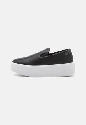 Zapatos negros tipo slip-on con parte superior de cuero suave, suela de plataforma blanca y recortes laterales para un uso fácil. Diseño minimalista y sin hardware visible.