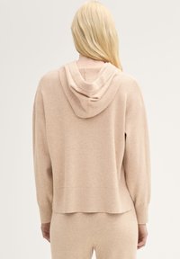 Felpa beige a maglia con silhouette rilassata, dotata di cappuccio con cordoncino e polsini a coste. Il materiale sembra morbido e testurizzato.