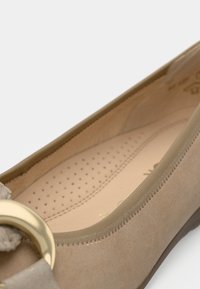 Nude ballerinasko laget av glatt semsket skinn med rund tå, med dekorativt gullfarget metalldetalj og perforert innersåle for pusteevne.