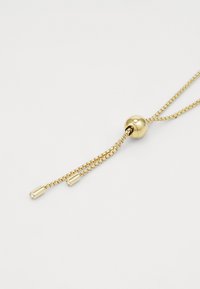 Collana regolabile dorata con una perla centrale e due catene sottili, ciascuna con estremità accentuate di forma cilindrica. Texture liscia e finitura lucida.